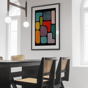 May include: A black framed print with a colorful abstract design featuring geometric shapes in shades of red, orange, yellow, green, blue, and purple. The print is hanging on a white wall above a black dining table with two chairs.