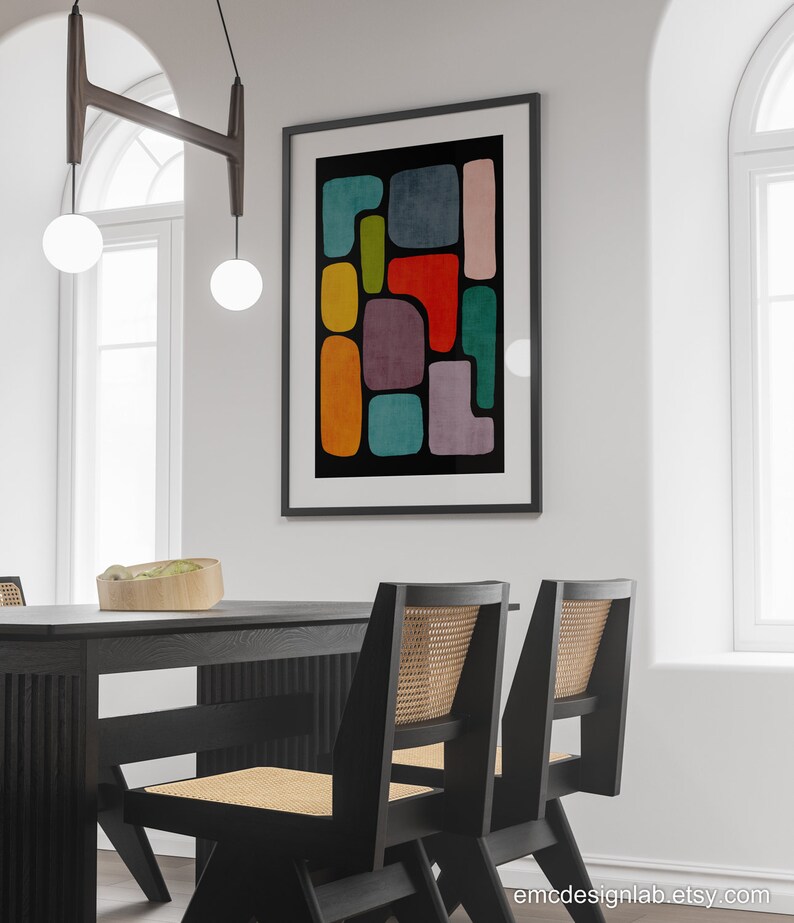 May include: A black framed print with a colorful abstract design featuring geometric shapes in shades of red, orange, yellow, green, blue, and purple. The print is hanging on a white wall above a black dining table with two chairs.