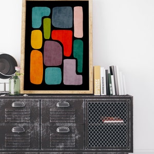 May include: Abstract geometric art print with colorful shapes on a black background. The print is framed in a light wood frame and is displayed on a metal cabinet with drawers.