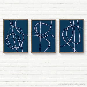 May include: Set of three abstract art prints with white lines on a dark blue background. The lines are simple and geometric, creating a modern and minimalist look.