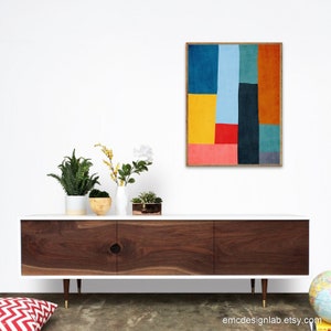 May include: A white mid-century modern media console with walnut wood doors and gold legs. The console is decorated with plants in white and brown pots, a small succulent in a copper pot, and a framed abstract art print with geometric shapes in blue, yellow, red, orange, and green.