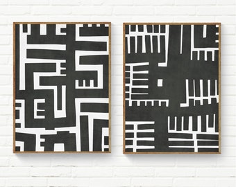 May include: Two framed abstract art prints. Each print has a black background with a white geometric design. The frames are a natural wood colour. The prints are displayed against a white brick wall.