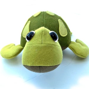 May include: A green felt stuffed turtle toy with black eyes. The turtle has a brown felt underside and a green felt shell with brown felt spots.
