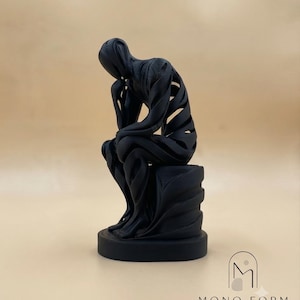 Puede incluir: Una escultura de color negro mate de una figura sentada en pose contemplativa, con un diseño de capas ahuecadas y estrías horizontales visibles. La figura descansa sobre una base circular, con el texto MONO FORM MODERN SCULPTURAL DECOR debajo.