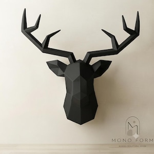 Pode incluir: Uma escultura de cabeça de veado montada na parede em preto mate, apresentando um design geométrico facetado com ângulos agudos e linhas limpas. A cabeça de veado inclui chifres grandes e ramificados e orelhas pontiagudas, com o texto MONO FORM MODERN SCULPTURAL DECOR.