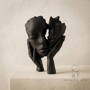 Peut inclure: Une sculpture noir mat représentant deux mains berçant un visage humain, avec une seconde forme de visage abstrait tenue sur le côté. La base présente le logo et le texte MONO FORM MODERN SCULPTURAL DECOR dans le coin inférieur droit.