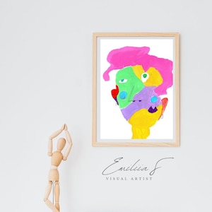 May include: A framed abstract portrait painting featuring vibrant blocks of pink, green, yellow, purple, and blue paint. The artwork is displayed in a light wood frame with the text Emilia F VISUAL ARTIST printed in black below the frame.