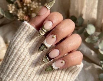 May include: Long almond-shaped nails featuring a French manicure style with olive green crocodile-textured tips. The design includes gold metallic bands, small gold studs, and white accents, creating a layered look on each nail tip.