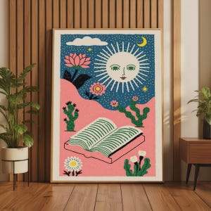 May include: A framed wall art print featuring a stylized sun with a face, a crescent moon, and stars in a dark blue sky above a pink landscape. The scene includes an open book, green cacti, and various flowers in shades of pink and white.