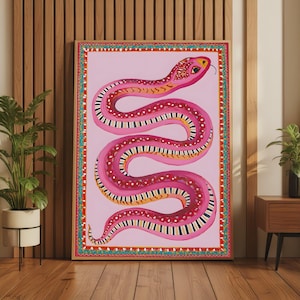 May include: A rectangular framed wall art print featuring a stylised pink snake with a patterned body of white dots and black and white stripes. The snake is set against a solid light pink background and enclosed within a decorative border.