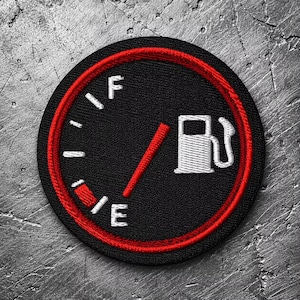 May include: A circular embroidered patch featuring a black fuel gauge design with a red border. The gauge includes white F and E letters, white tick marks, a red needle pointing to the middle, and a white gas pump icon on the right side.