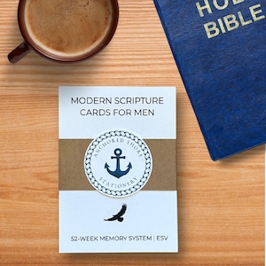 May include: A deck of white cards titled MODERN SCRIPTURE CARDS FOR MEN with a brown band featuring a blue anchor logo inside a rope circle. The cards include a black eagle silhouette and the text 52-WEEK MEMORY SYSTEM | ESV at the bottom.