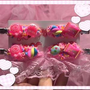 Könnte beinhalten: Vier Haarspangen auf einer weißen Trägerkarte, verziert mit rosa, zuckergussartiger Textur, bunten Streuseln und kleinen Süßigkeiten-Anhängern wie Lollis, Eiscreme, Marshmallows und rosa Verpackungen mit der Aufschrift Sweet.