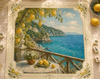 May include: A square placemat featuring a printed coastal landscape painting of a Mediterranean terrace overlooking a blue sea, framed by a decorative border with lemon illustrations. The scene includes a stone table with lemons.