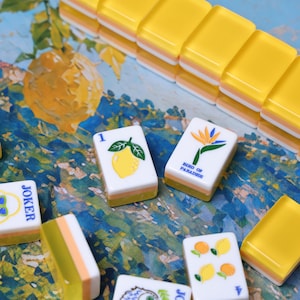 May include: A set of rectangular mahjong tiles with translucent yellow and white layered bases. The tiles feature colorful illustrations including a yellow lemon with the number 1, a bird of paradise flower, and the text "BIRD OF PARADISE".