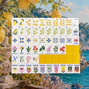 May include: A set of white mahjong tiles arranged in a grid, featuring colorful illustrations of lemons, plants, flowers, geometric patterns, and animals. The tiles include text labels like BAM, CRAK, and JOKER, with some blank yellow tiles included.
