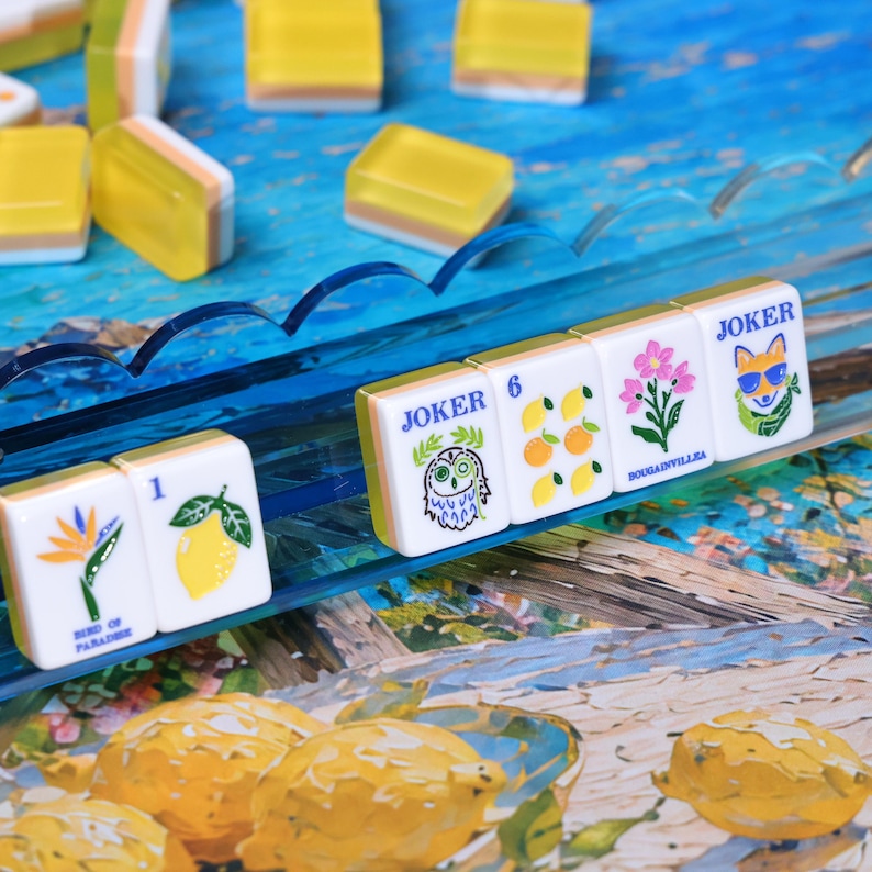 May include: A set of rectangular mahjong tiles featuring colorful illustrations of a bird of paradise, a lemon, an owl, citrus fruits, bougainvillea flowers, and a fox wearing sunglasses, with some tiles labeled Joker, 1, 6, and Bougainvillea.