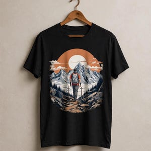Puede incluir: Una camiseta negra de manga corta con un estampado gráfico circular de un excursionista con mochila caminando por un sendero rocoso hacia montañas nevadas bajo un gran sol naranja, con pinos y dos bastones de senderismo verticales.