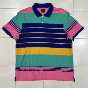 May include: A short-sleeve polo shirt featuring horizontal stripes in pink, teal, navy blue, and yellow. The shirt has a solid navy blue collar, a two-button placket, and a J.Crew brand label on the inside neck. The sleeves have navy blue stripes.