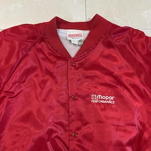 May include: A bright red satin bomber jacket featuring a ribbed collar and snap-button front closure. The chest displays the white embroidered text Mopar Performance with a logo. A Hartwell brand label is visible inside the neckline.