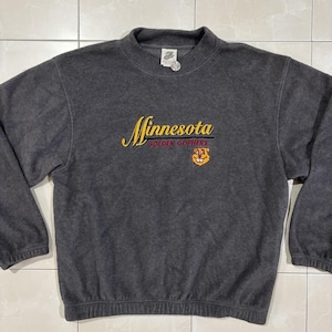May include: A charcoal grey long-sleeve fleece sweatshirt featuring the embroidered text Minnesota Golden Gophers in yellow and maroon, accompanied by a small embroidered gopher mascot graphic on the front centre chest area.