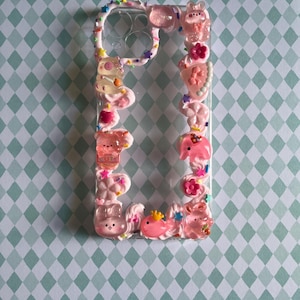 Peut inclure: Une coque de t&eacute;l&eacute;phone transparente d&eacute;cor&eacute;e d'une texture rose fa&ccedil;on cr&egrave;me fouett&eacute;e, orn&eacute;e de divers charms en r&eacute;sine color&eacute;s, notamment des ours translucides, des fleurs, des &eacute;toiles et des petites paillettes autour du contour.