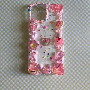 Peut inclure: Une coque de t&eacute;l&eacute;phone transparente d&eacute;cor&eacute;e d'une texture ressemblant &agrave; de la cr&egrave;me fouett&eacute;e blanche, de vermicelles color&eacute;s et de divers charms en r&eacute;sine rose, dont un n&oelig;ud, un c&oelig;ur avec une fleur, un ours et d'autres petites figurines.