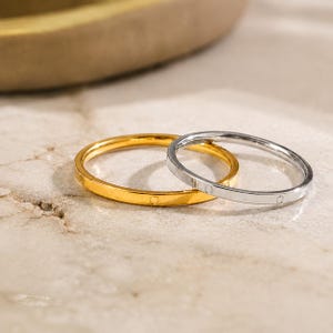 Puede incluir: Dos anillos finos apilables, uno en tono dorado pulido y otro en tono plateado pulido. Cada anillo presenta un diseño de banda plana y lisa con pequeñas hendiduras circulares espaciadas uniformemente grabadas en la superficie exterior.