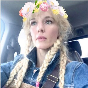 Puede incluir: Una mujer con el pelo rubio trenzado, lleva una chaqueta vaquera y un mono. Lleva un filtro de corona de flores sobre la cabeza.