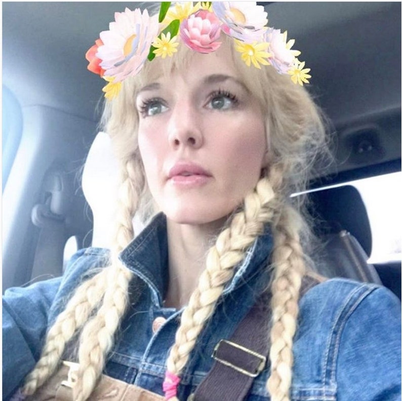 Puede incluir: Una mujer con el pelo rubio trenzado, lleva una chaqueta vaquera y un mono. Lleva un filtro de corona de flores sobre la cabeza.