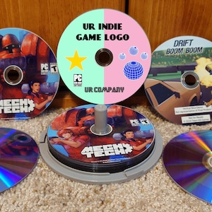 May include: A collection of five circular PC game discs featuring various designs. One disc displays the text UR INDIE GAME LOGO and UR COMPANY. Two discs feature the title MECH TECH with character art. One disc shows DRIFT BOOM BOOM.