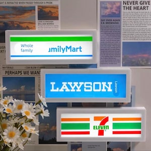 May include: Three rectangular light boxes featuring convenience store logos. The top box displays the FamilyMart logo with green and blue stripes. The middle box shows the blue Lawson logo. The bottom box features the 7-Eleven logo with orange, green, and red stripes.