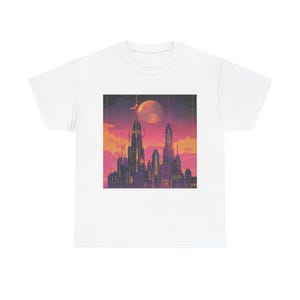 May include: A white t-shirt featuring a centered graphic print of a futuristic cityscape at sunset. The illustration displays tall, slender skyscrapers against a vibrant orange and purple sky with a large, glowing moon positioned above the buildings.