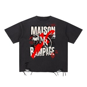 May include: A black short-sleeved t-shirt featuring a distressed graphic print with the text MAISON RAMPAGE and MR 08. The design includes a large red brushstroke across the centre, and the bottom hem has intentional rips and frayed threads.