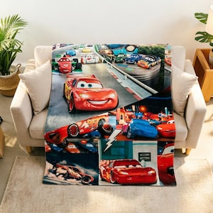 May include: A soft throw blanket featuring a collage of scenes from the Cars movie franchise, prominently displaying the red race car Lightning McQueen with the number 95, alongside various other colourful animated vehicles on a racetrack.
