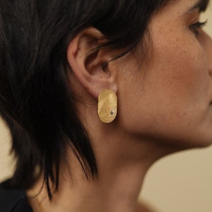 May include: A pair of gold oval-shaped earrings with a textured surface and a small diamond-shaped stone in the center.