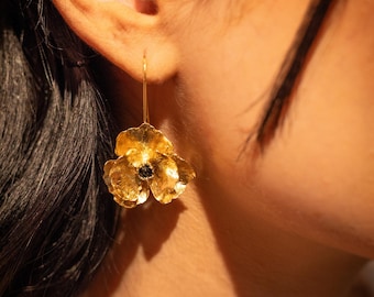 Puede incluir: Pendientes colgantes de oro en forma de flor con una piedra central negra.