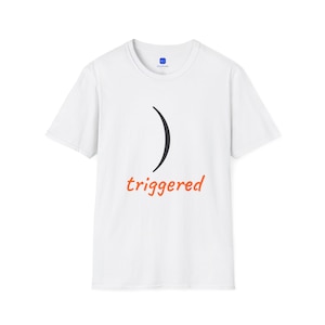 May include: A white short-sleeved t-shirt featuring a black curved line graphic positioned above the orange lowercase text "triggered" centered on the chest. The garment has a crew neckline and a standard fit with a blue logo on the inner neck label.