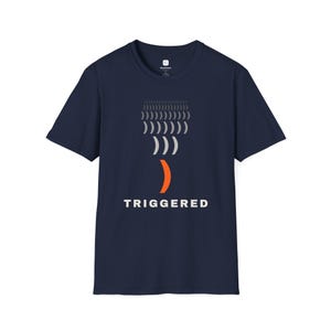 May include: A navy blue short-sleeve t-shirt featuring a graphic design of multiple gray parentheses arranged in a vertical column, ending with a single larger orange parenthesis at the bottom, with the word TRIGGERED printed in white below.