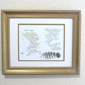 May include: A framed artwork featuring a poem with calligraphy text and a feather illustration. The gold-colored frame surrounds a white matting, with the poem's text in black ink. The artwork is mounted on a wall.