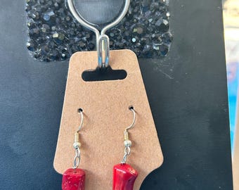 May include: A pair of drop earrings featuring a red, porous, rectangular bead topped with a silver-tone rhinestone spacer and a yellow, teardrop-shaped glass bead with red and orange swirls, suspended from silver-tone metal earring hooks.