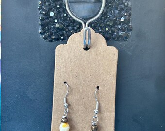 May include: A pair of dangle earrings featuring silver-toned hooks, small metallic beads, and larger yellow and white spherical beads. The earrings are displayed on a rectangular brown card, which is suspended from a silver hook labelled GF.
