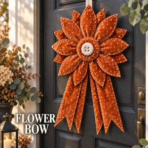 May include: A decorative fabric flower bow in a burnt orange hue with white polka dots. The design features layered, petal-like fabric segments arranged in a circular pattern, centered with a large, round, cream-colored button with two holes.