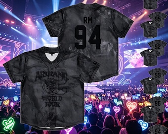 Op de afbeelding: Een zwart honkbalshirt met korte mouwen, knoopsluiting en een mesh-textuur. De voorzijde is voorzien van de tekst ARIRANG WORLD TOUR. De achterzijde toont de letters RM en het getal 94 in een groot zwart lettertype met een subtiel patroon.