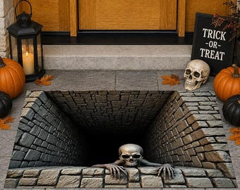 Op de afbeelding: Een rechthoekige deurmat met een 3D-optische illusie van een diepe, donkere stenen put. Een realistische menselijke schedel met skeletachtige handen is aan de rand van de put geplaatst en lijkt uit de donkere afgrond naar voren te klimmen.