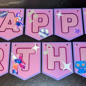 以下が含まれることがあります： グリッターピンクの文字でHAPPY BIRTHDAYと綴られた紫色のペナントバナー。各ペナントにはK-POPデーモンハンターズのキャラクターグラフィック、音符、星、きらめきが描かれています。最後のペナントにはK-POP DEMON HUNTERSというテキストが含まれています。