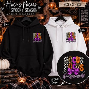 May include: A black hoodie and a white hoodie, each featuring a left chest graphic with the text Hocus Pocus Spooky Season. The design includes a purple bow, bats, and checkered and orange star patterns. The hoodies have drawstrings and front pockets.
