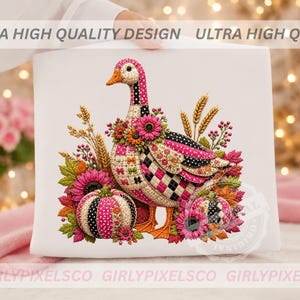 May include: A white t-shirt featuring a colorful graphic of a goose decorated with pink, black, and white patterns, surrounded by autumn elements including orange pumpkins, wheat stalks, pink sunflowers, and vibrant fall leaves.