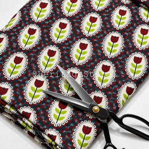 May include: Fabric featuring a repeating pattern of red tulips with green stems inside white oval frames with small flower borders, set against a dark blue and red checkered background. A pair of black metal scissors rests on the fabric.