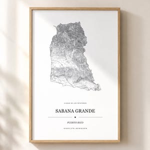 May include: A framed wall art print featuring a detailed black and white topographic map of Sabana Grande, Puerto Rico. The text reads CIUDAD DE LOS PETATEROS, SABANA GRANDE, PUERTO RICO, and the coordinates 18°05'01.27"N | 66°56'36.00"W.